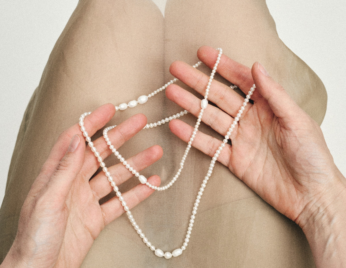 Hands holding the Ondumi freshwater pearl sautoir over sheer beige fabric - daure collection