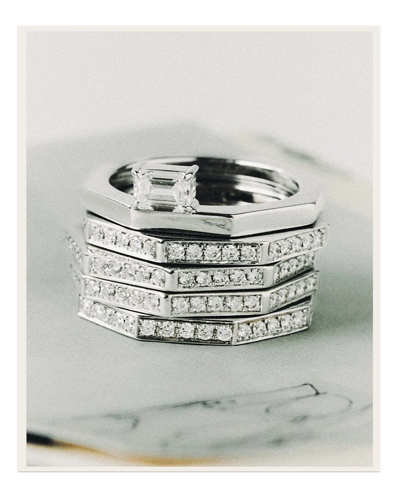 Stack of five 18K white gold octagonal rings: an east-west emerald-cut lab-grown diamond solitaire on top of four pavé lab-grown diamond eternity bands, on a marble surface. Daure collection