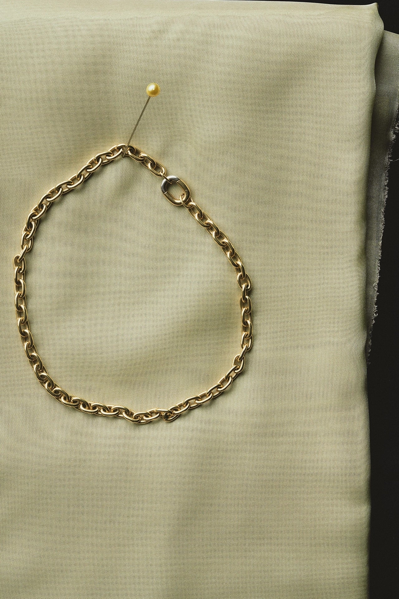 Yellow gold chain link bracelet pinned on cream fabric cushion - Daure collection