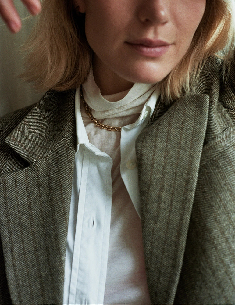 Woman wearing a yellow gold chain necklace layered over a white shirt and herringbone wool blazer – daŭre collection
