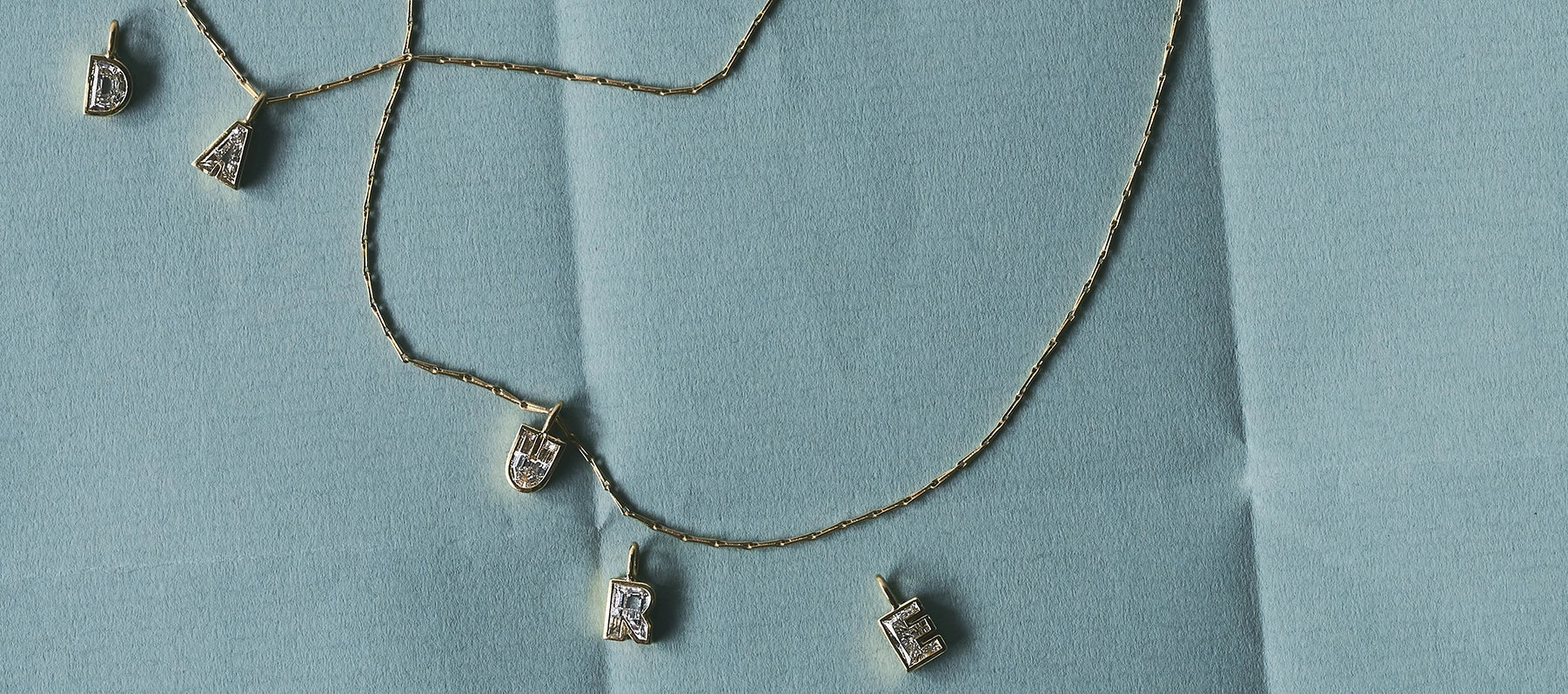18k yellow gold diamond letter pendants spelling DAURE layered on a fine chain necklace — daŭre collection