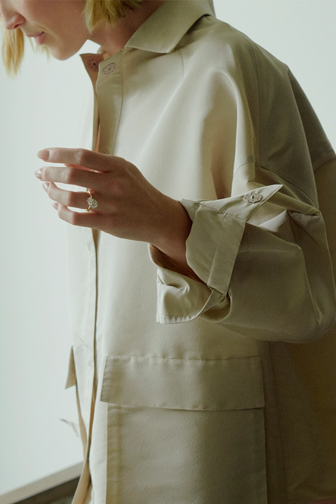 Woman wearing yellow gold diamond ring on hand in beige coat - Daure collection