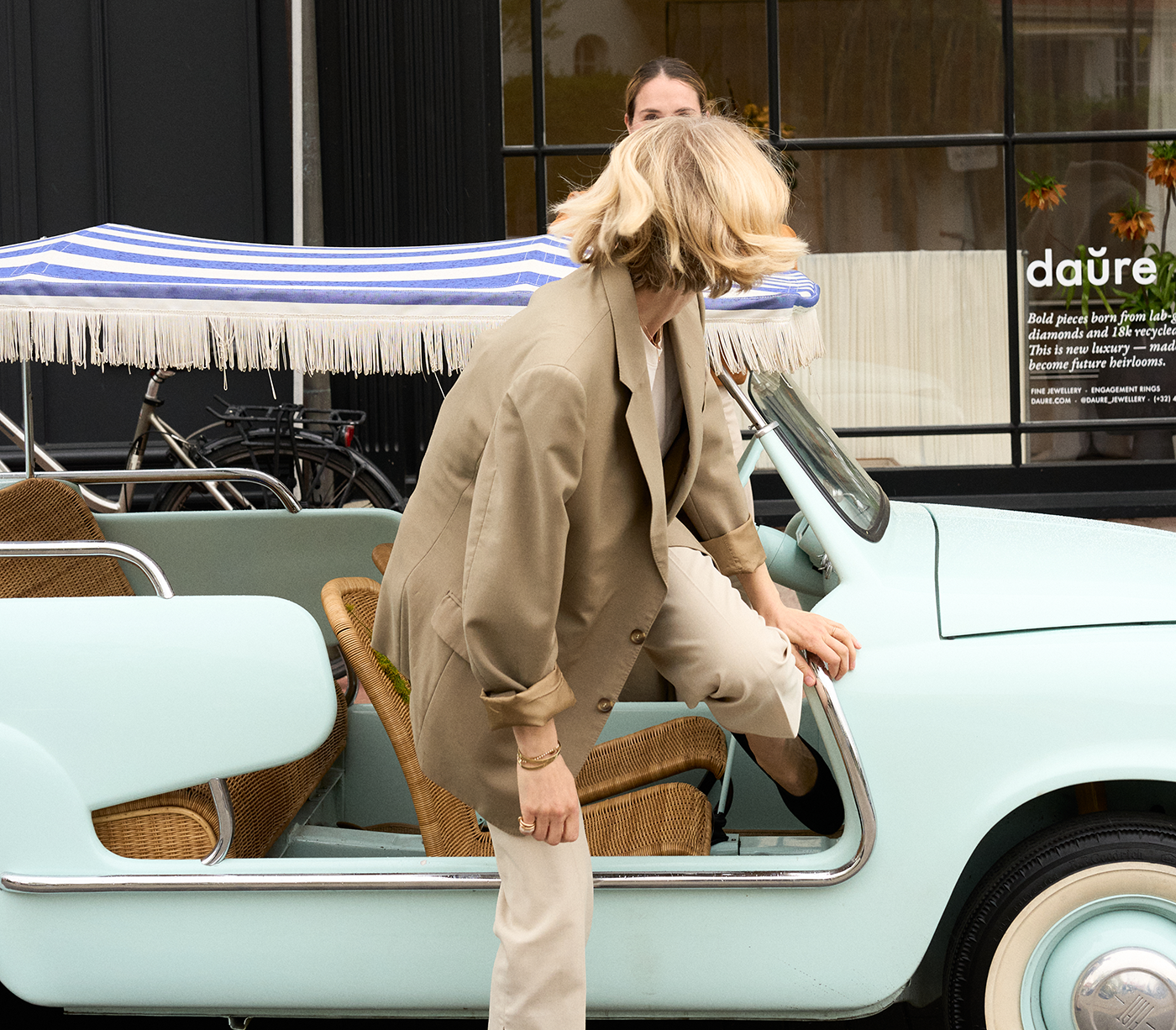 Woman getting into a vintage light blue car with a striped canopy.