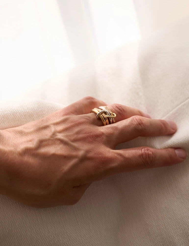 Close-up of a woman's hand wearing stacked sculptural yellow gold rings on a white fabric background – daŭre collection