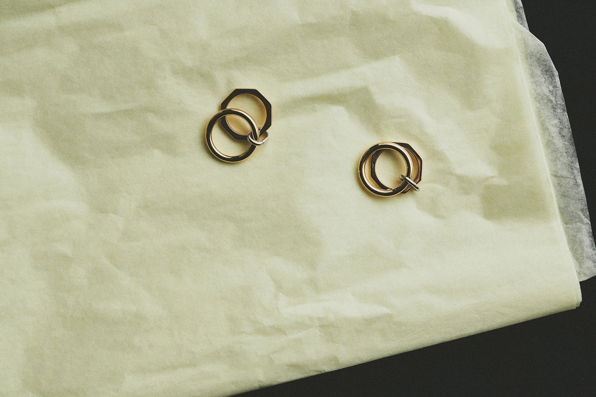 Pair of yellow gold octagonal interlocking hoop earrings flat lay on cream tissue paper - Daure collection