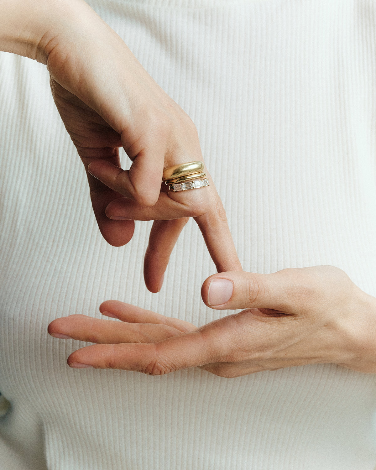 Hand wearing a stack of yellow gold rings with an emerald-cut lab-grown diamond band - Daure collection